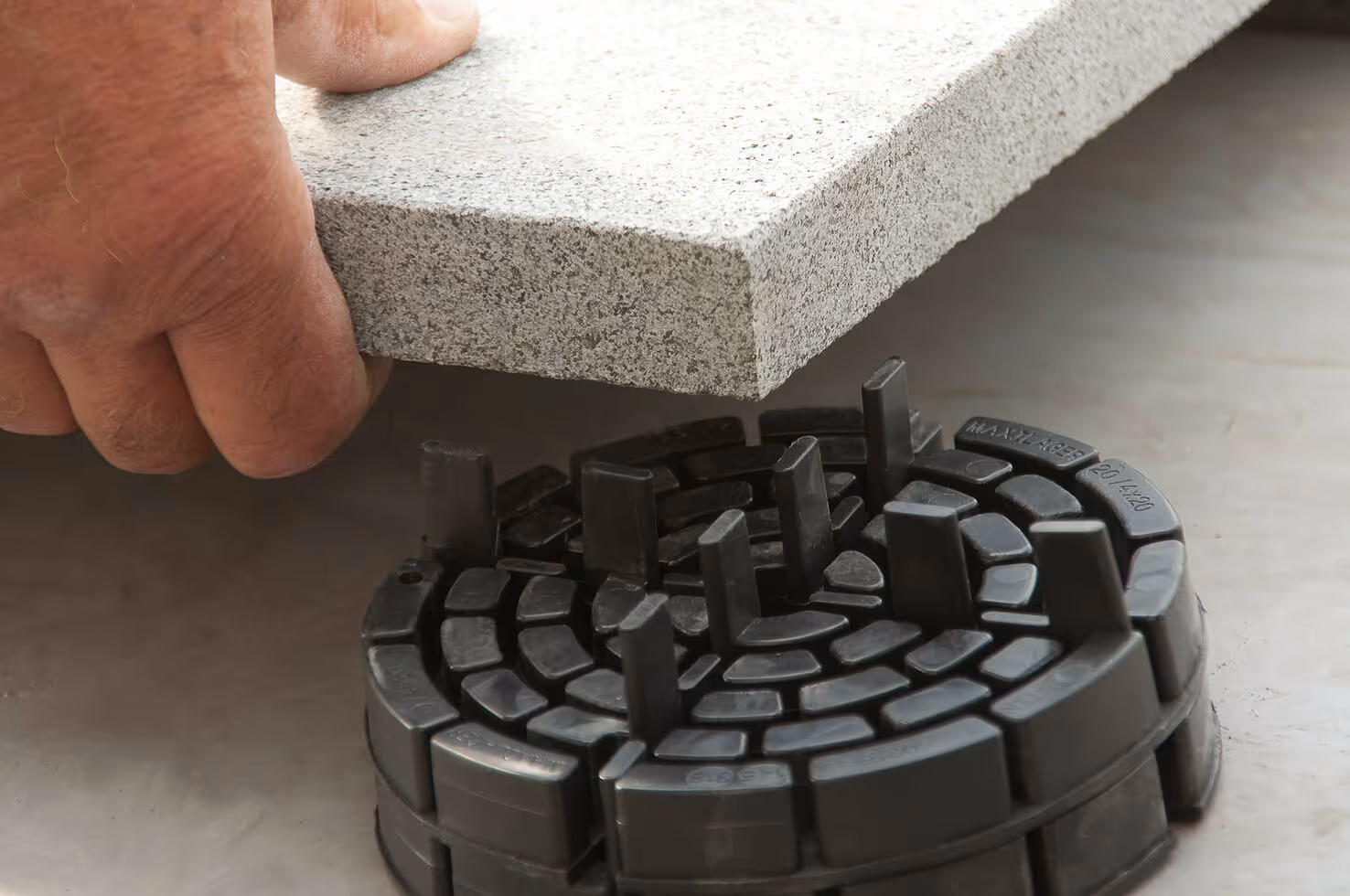 Close-up of a hand placing a gray tile on a black adjustable pedestal for flooring support.